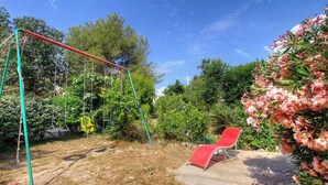 Ein Garten mit Schaukel, rotem Stuhl und dichtem Grün.