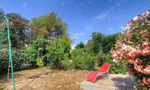Ein Garten mit Schaukel, rotem Stuhl und dichtem Grün.