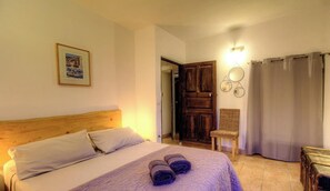 A bedroom with a wooden headboard, a bed with white linens, a framed picture on the wall, a wicker chair, and a curtain. - The Milky Way - ERBAJOLO (ERBAJOLO)