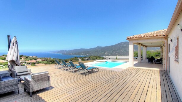 Eine Holzterrasse mit Liegestühlen und einem Pool mit Blick auf eine Küstenlandschaft.