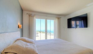 Ein Schlafzimmer mit Bett, Fernseher und Fenster mit Meerblick.