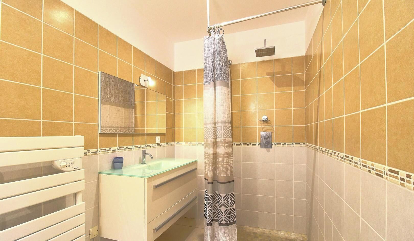 Une salle de bain avec un lavabo en verre, un miroir, une douche avec un rideau et des murs carrelés.