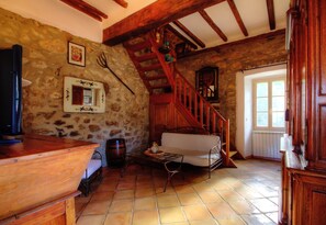 Ein rustikales Interieur mit Steinwand, Holzbalken, einer Treppe, einem weißen Sofa und einem Holztisch.