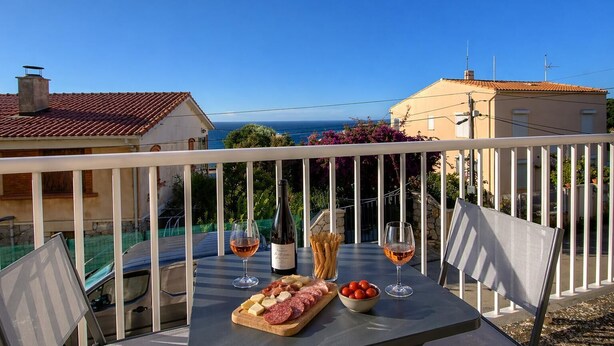 A balcony with a table set for a meal, a bottle of wine, and a view of the sea. - Casa Margone - CALVI (CALVI)