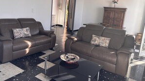 A living room with two brown leather sofas, a glass coffee table, and a patterned throw pillow. - Casa Margone - CALVI (CALVI)