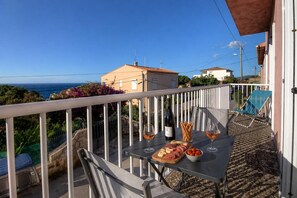 Ein Balkon mit Tisch, gedecktem Essen, einer Weinflasche und einem Stuhl.