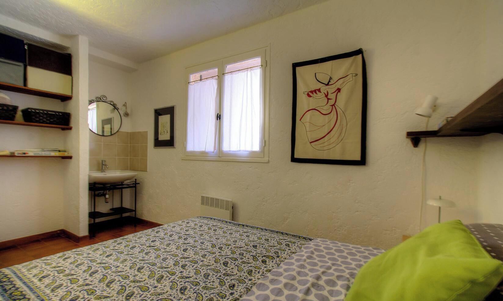 A bedroom with a bed, a window, a radiator, a mirror, and a picture on the wall.