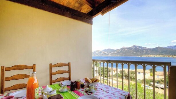 Un balcón con una mesa lista para el desayuno, con vistas a un paisaje costero y montañas.