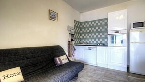 Un espacio habitable compacto con sofá, una pequeña cocina que incluye microondas, horno y lavavajillas, y un salpicadero de espinilla.