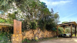 Un muro de piedra, una puerta de madera y un área de estar al aire libre techada con mesas y sillas.
