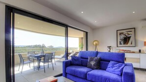 Ein modernes Wohnzimmer mit einem blauen Sofa, einem Esstisch mit Stühlen und einem Balkon mit Blick.