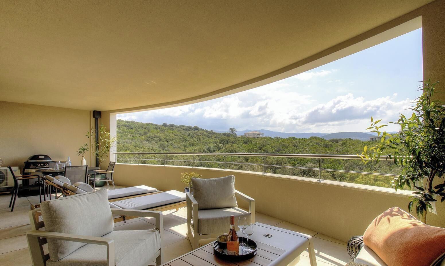 A balcony with outdoor seating, a grill, and a view of a green landscape.