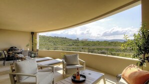 Ein Balkon mit Sitzgelegenheit im Freien, einem Grill und Blick auf eine grüne Landschaft.