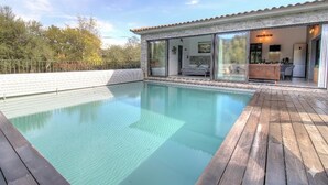 En swimmingpool med ett trädäck, en inglasad uteplats och utsikt över de omgivande träden.