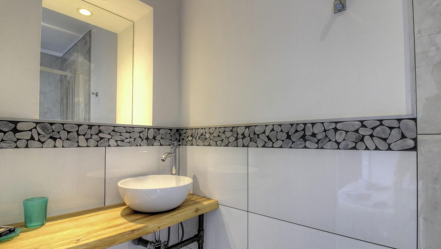 Un bany amb un lavabo blanc, una prestatgeria de fusta, un mirall i un respatller de rajola.