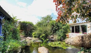 Ein Garten mit Teich, Steinen und einem Gebäude mit Balkon.