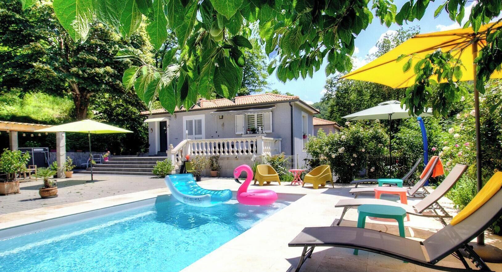 Piscina com brinquedos infláveis, área de estar ao ar livre e uma casa ao fundo.