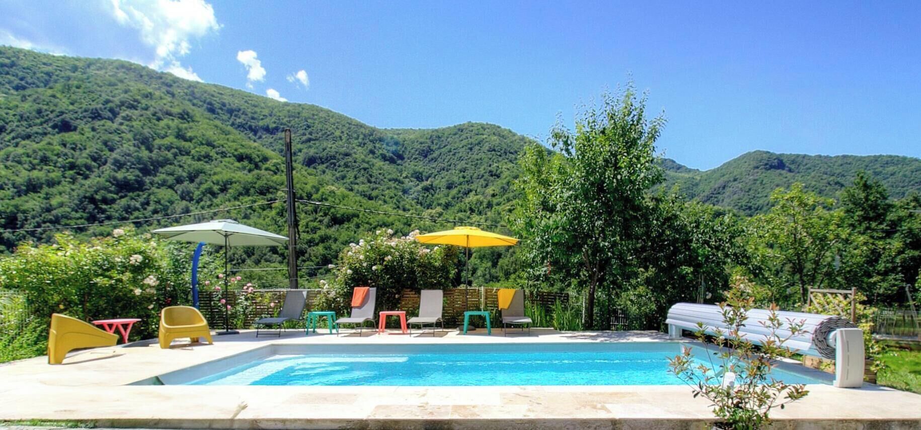 Une piscine entourée d’une végétation luxuriante et de montagnes, avec des chaises longues et des parasols.