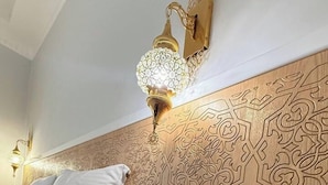 Ett hotellrum med en sänggavel i trä, en telefon vid sängen, ett vägguttag och en dekorativ lampa.