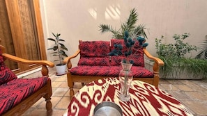 A room with a patterned sofa, a wooden chair, a small table, and a potted plant.