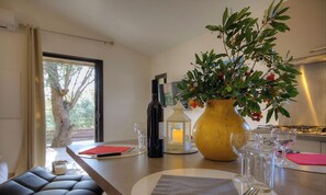 A dining area with a table set for two, a vase with green foliage, a candle, and a bottle of wine. - Bergerie de Petralonga2 (SOTTA)