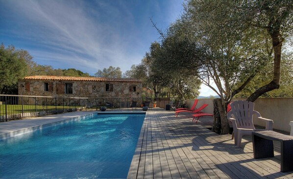 A swimming pool with a stone building in the background, outdoor seating, and trees. - Bergerie de Petralonga2 (SOTTA)