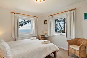 Ein Schlafzimmer mit Bett, Stuhl, Schreibtisch und Meerblick.