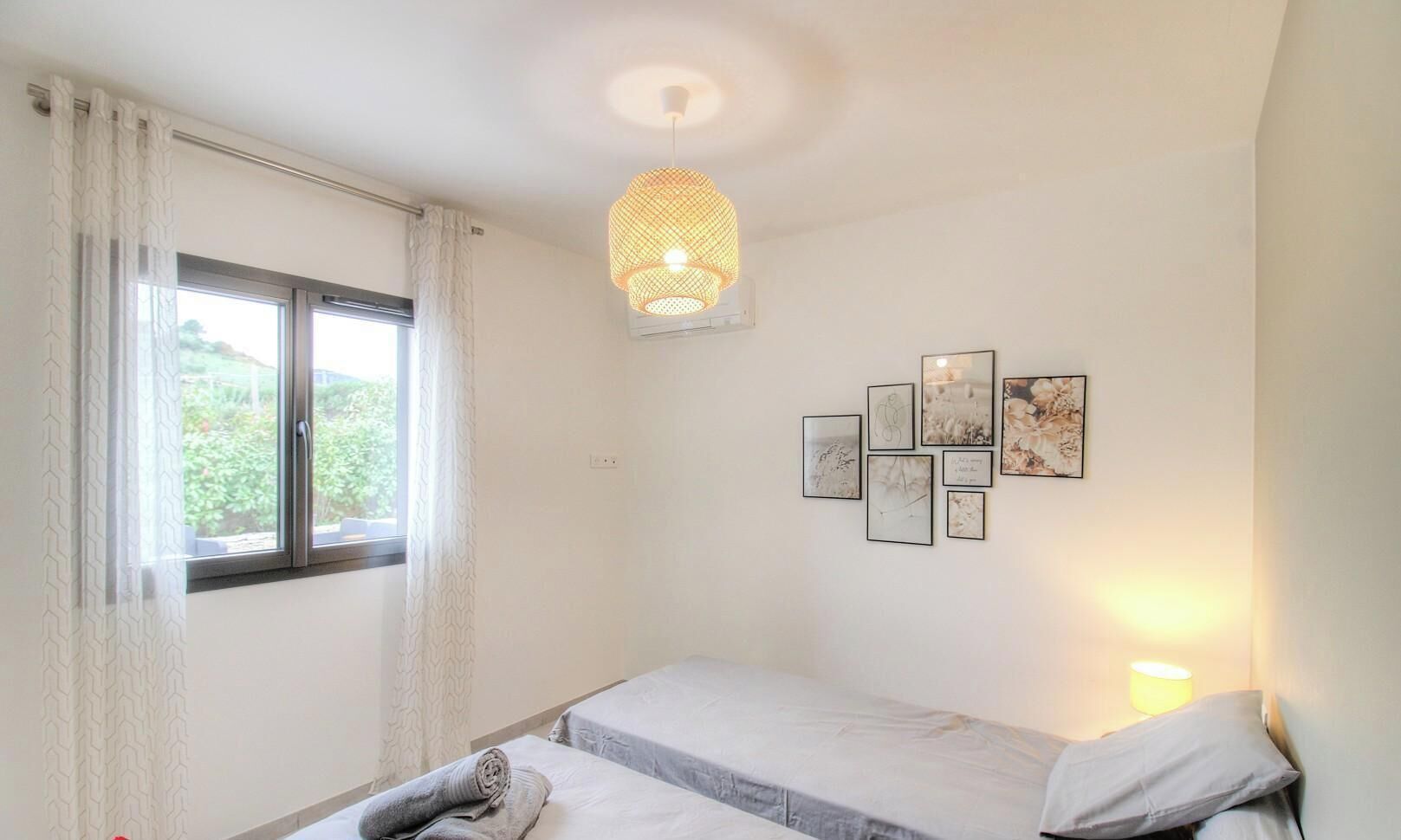 A bedroom with a bed, a window with curtains, a wall-mounted light, and framed pictures.