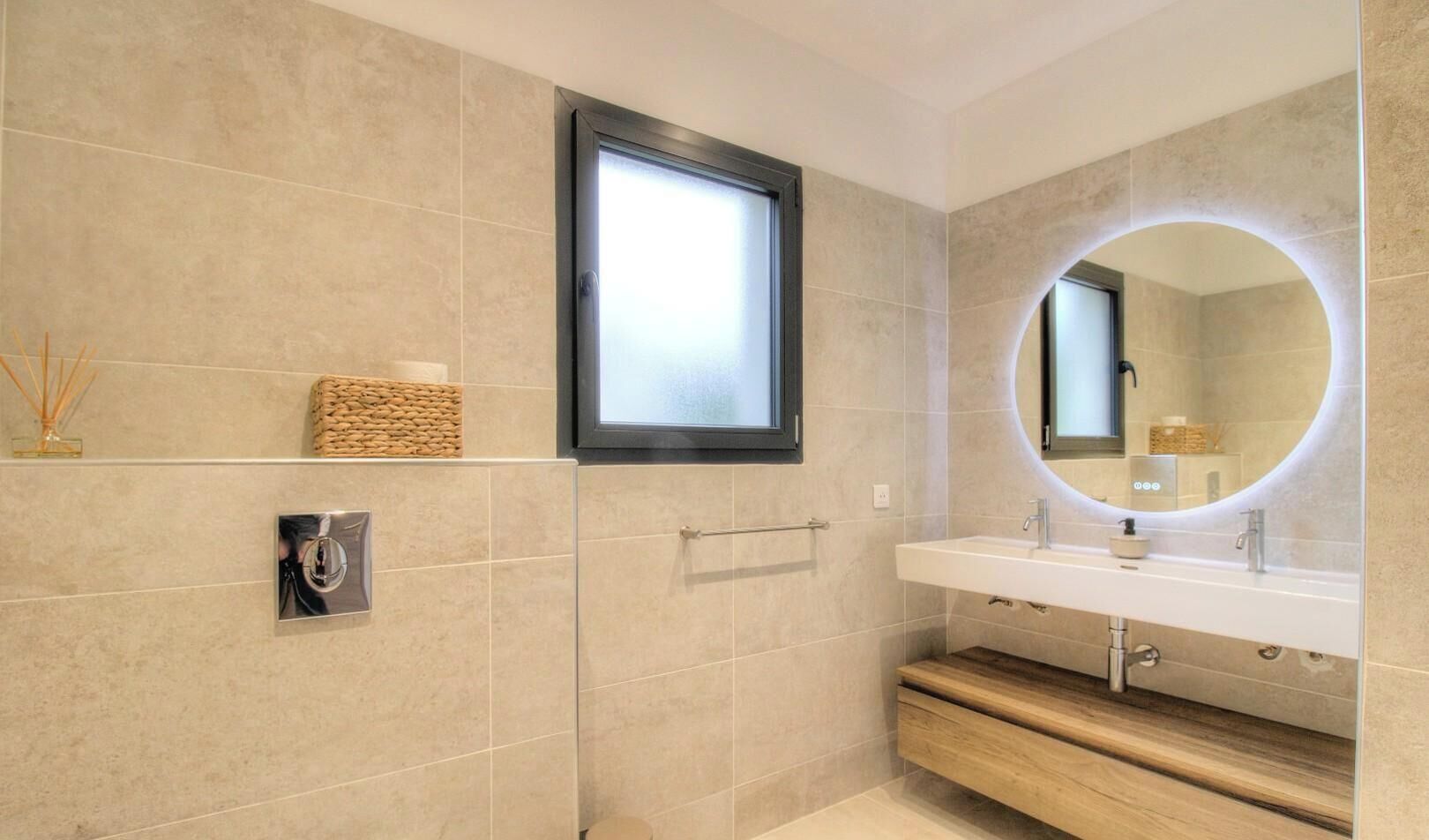 A modern bathroom with a large mirror, a window, and a wooden vanity.