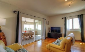 Ein Wohnzimmer mit einer Couch, einem Fernseher und einem Essbereich mit Stühlen und einem Tisch.