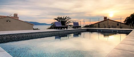 A swimming pool with lounge chairs, a view of the sea, and a sunset.