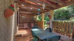 Un patio exterior con una pérgola de madera, una mesa, sillas y una maceta decorativa.