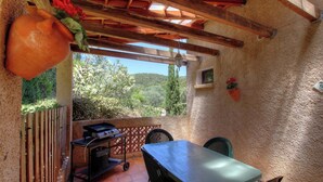 Un patio techado con una parrilla, una mesa, sillas y vistas al verdor.