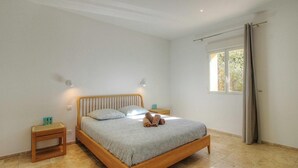Een slaapkamer met een houten bed, twee nachtkastjes, een raam met gordijnen en uitzicht op groen.