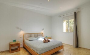 Ein Schlafzimmer mit einem hölzernen Bett, zwei Nachttischen, einem Fenster mit Vorhängen und Blick ins Grüne.