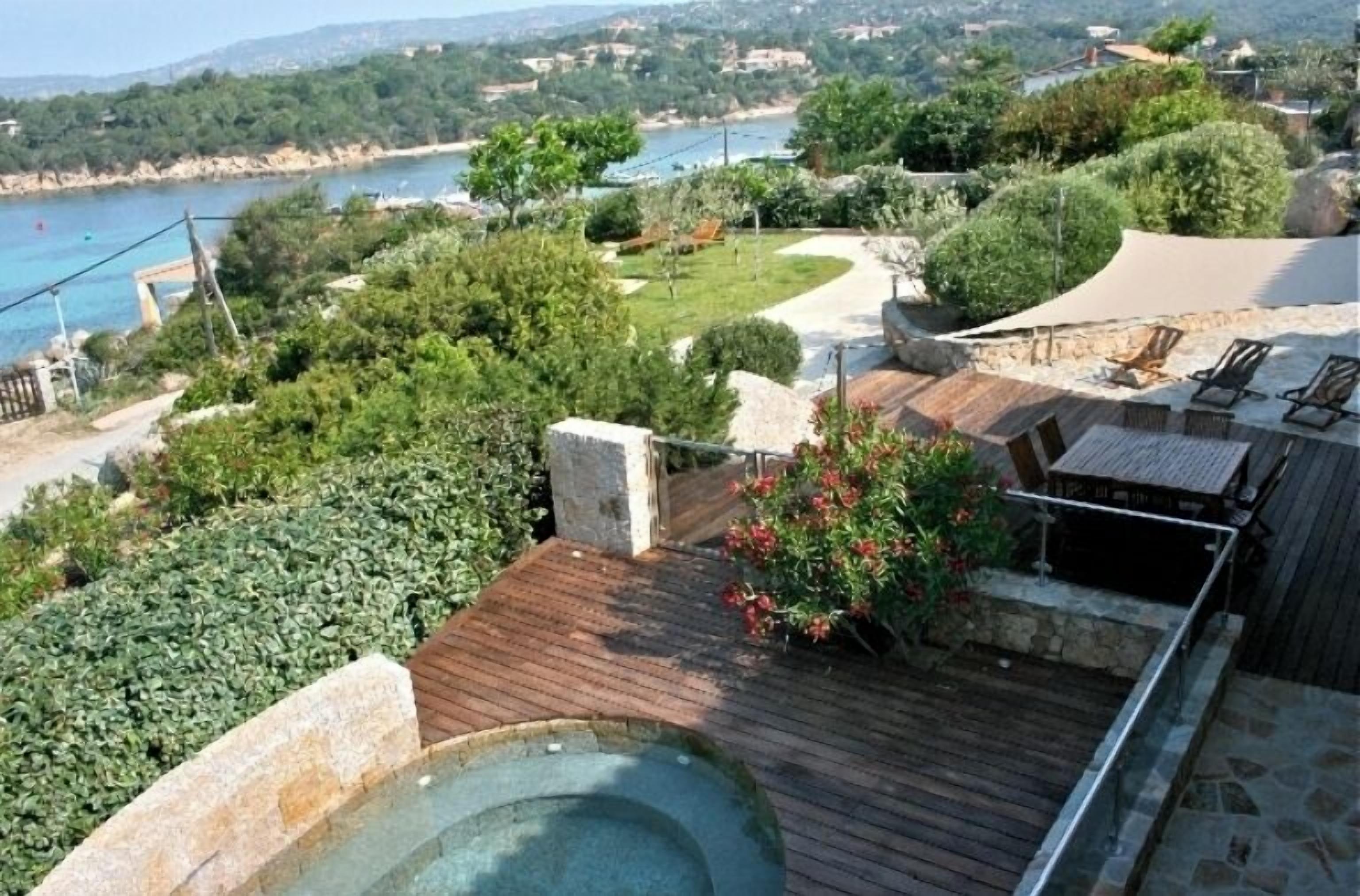 Zona de piscina con muelle de madera, estructura de piedra y vista al paisaje costero.