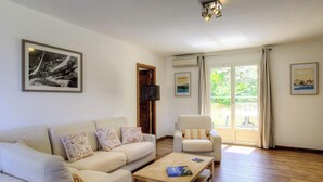 Una sala de estar con sofá, sillón, mesa de centro y un ventanal con cortinas.