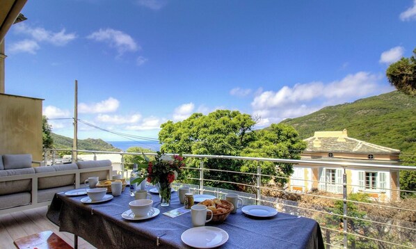 Une table à manger installée à l’extérieur, offrant une vue sur une colline et un bâtiment.