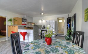 Una cocina moderna con armarios blancos, encimera de granito y un comedor con una mesa dispuesta para dos personas.