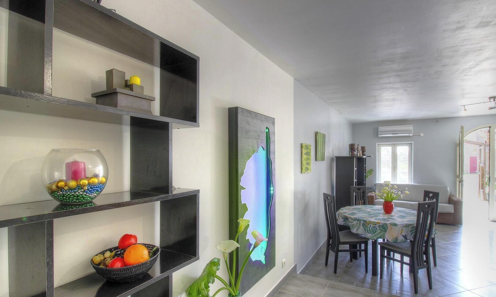 A dining area with a table and chairs, a wall-mounted shelf with decorative items, and a large abstract painting.