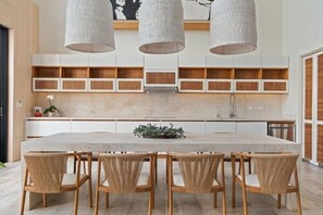 A modern kitchen with a central island, built-in cabinets, and a dining area with chairs. - Casa Mirage (Hacienda Pinilla)