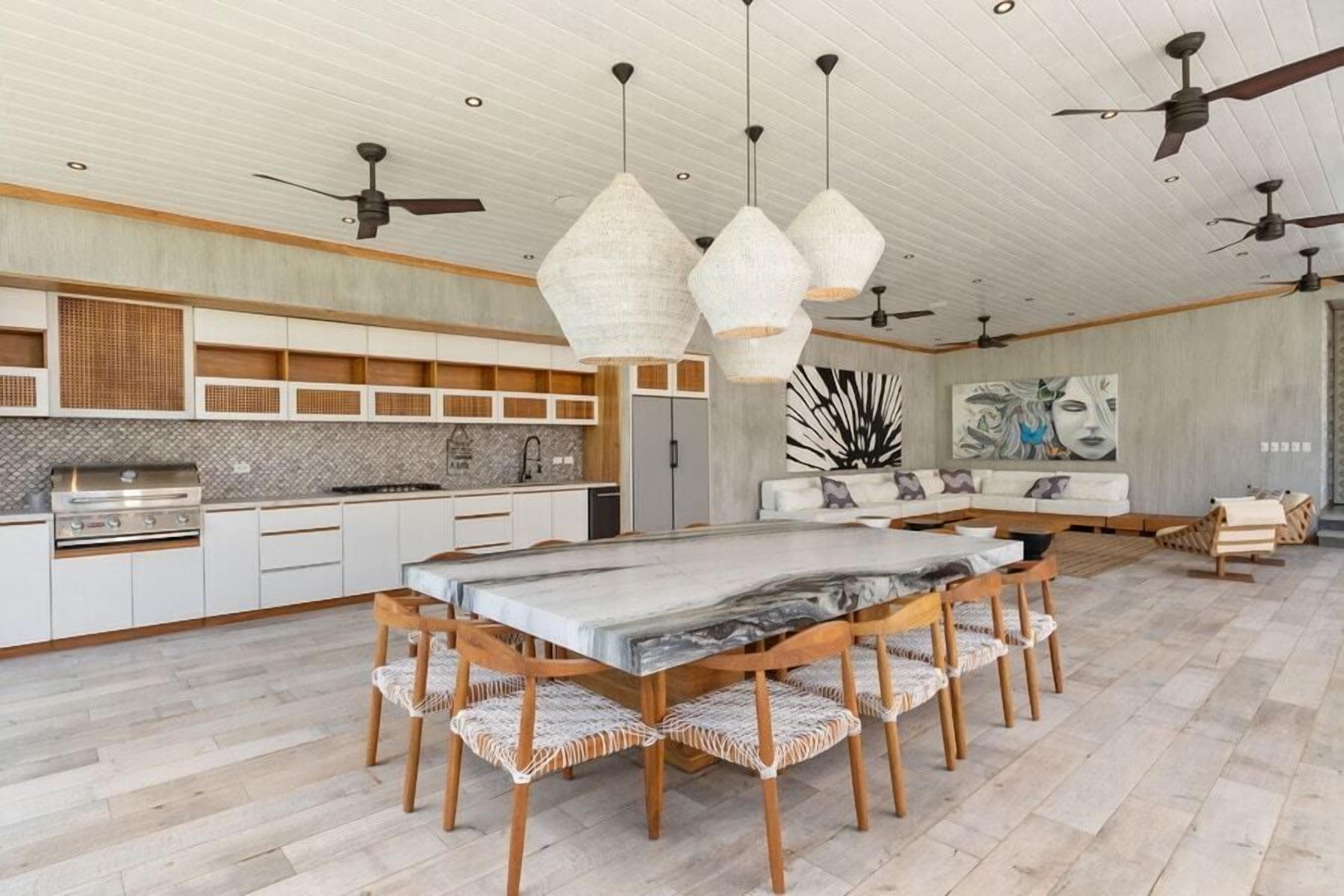 A modern kitchen with a central island, pendant lighting, and a dining area with a marble table.