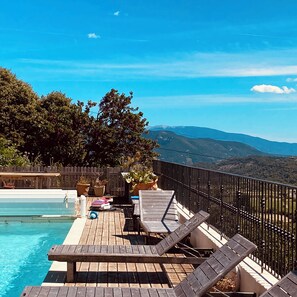 Eine Holzterrasse mit Liegestühlen mit Blick auf einen Pool und Berge.