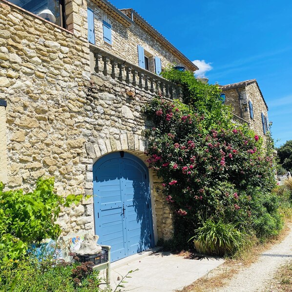 Ein Steinhaus mit einer blauen Tür und einem Garten mit rosa Blumen.