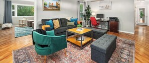 A living room with a sofa, coffee table, and ottoman, a desk with a computer, and a window with curtains. - Sandstone Hollow King Suite, Office, Fenced Yard (Fort Collins)