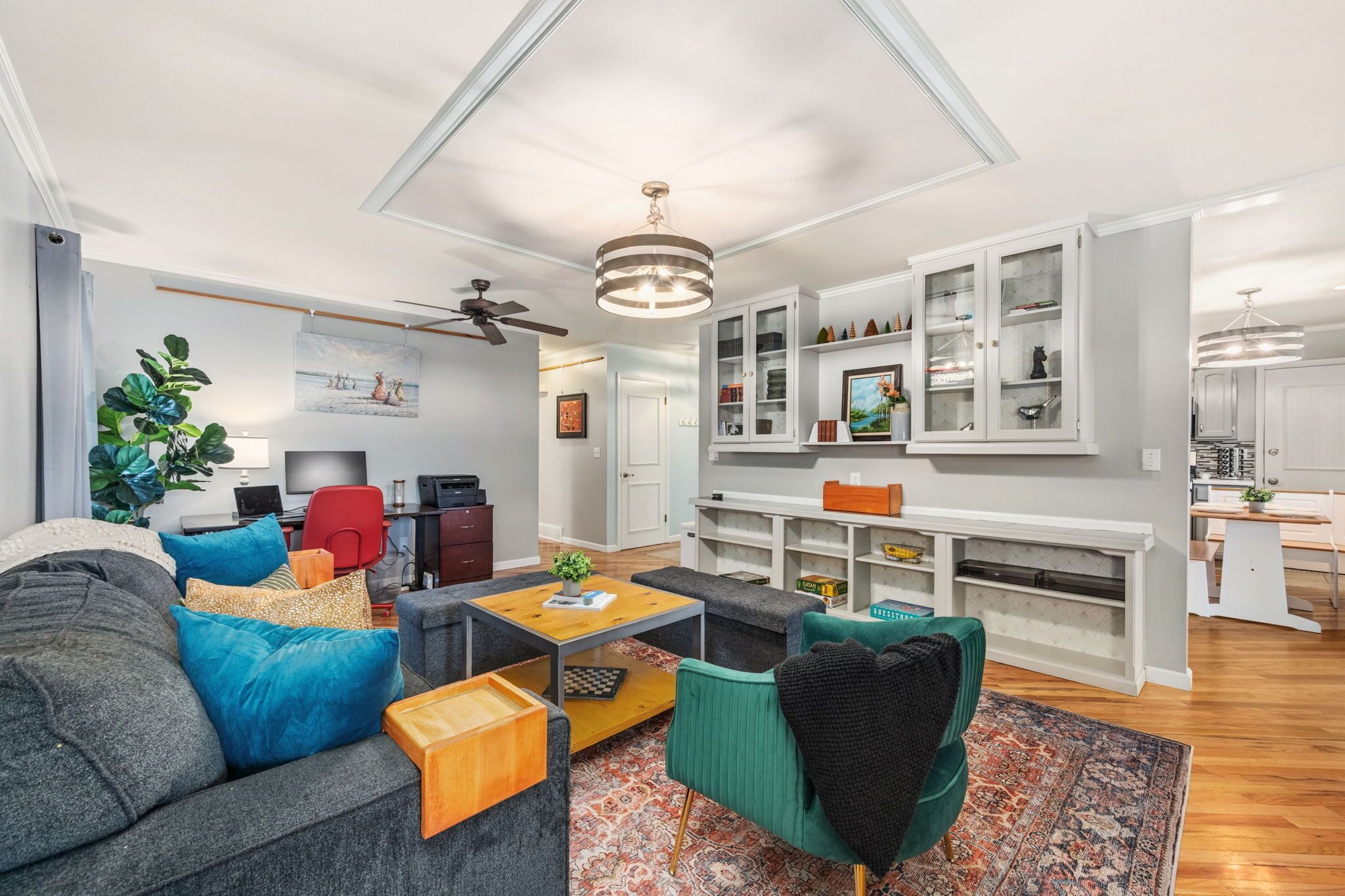 A modern living room with a sofa, coffee table, and a TV. There are cabinets with glass doors and a ceiling fan.