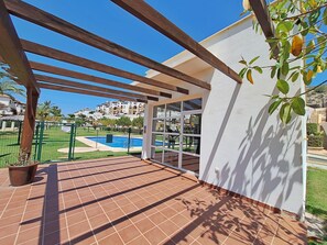 Ein überdachter Patio-Bereich mit Pool, Holz-Pergola und Blick auf einen Wohnkomplex.