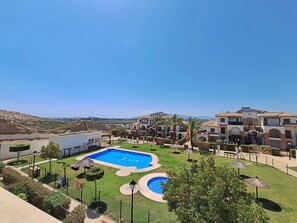 Ein Resort mit einem zentralen Schwimmbad, mehreren Gebäuden mit Balkonen und einer hügeligen Landschaft im Hintergrund.