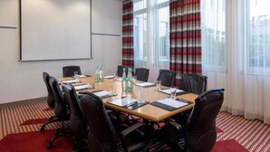 Ein Konferenzraum mit einem großen Tisch, Stühlen, einer Projektionsleinwand und großen Fenstern mit Vorhängen.