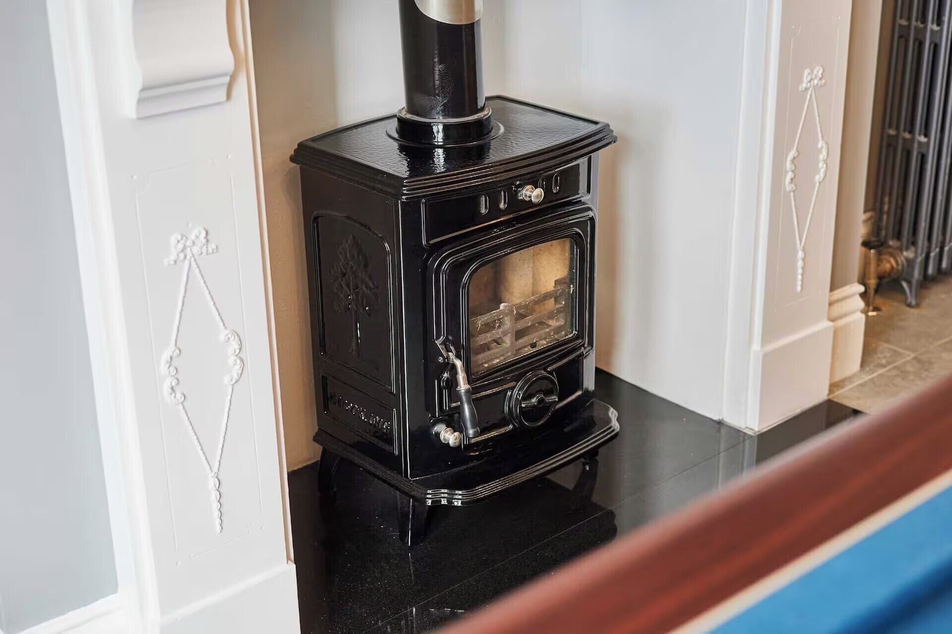 A black wood-burning stove with a glass door, set against a white wall with decorative molding.